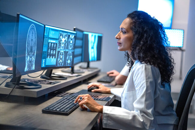 Hispanic woman working on computer. Female doctor analyzing medical scan result.