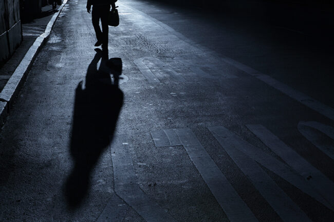 Lone man walks up street night shadows