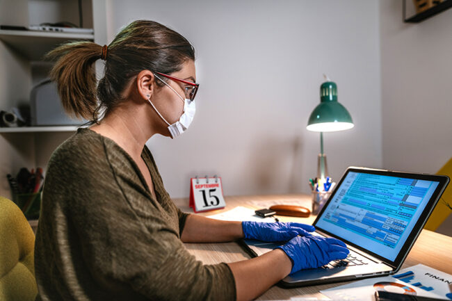 Woman filling online tax form, wearing face mask and gloves to protect from virus infection