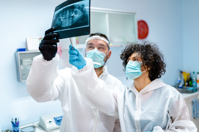 Dentis with a help of a dentist assistant brainstorming prosthetic solution for a patient while looking at X-ray image